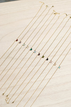 Gold necklaces with small colored pendants on a light wooden surface
