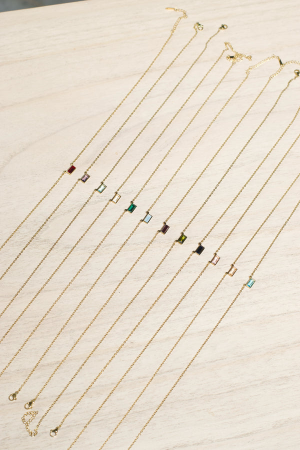 Gold necklaces with small colored pendants on a light wooden surface