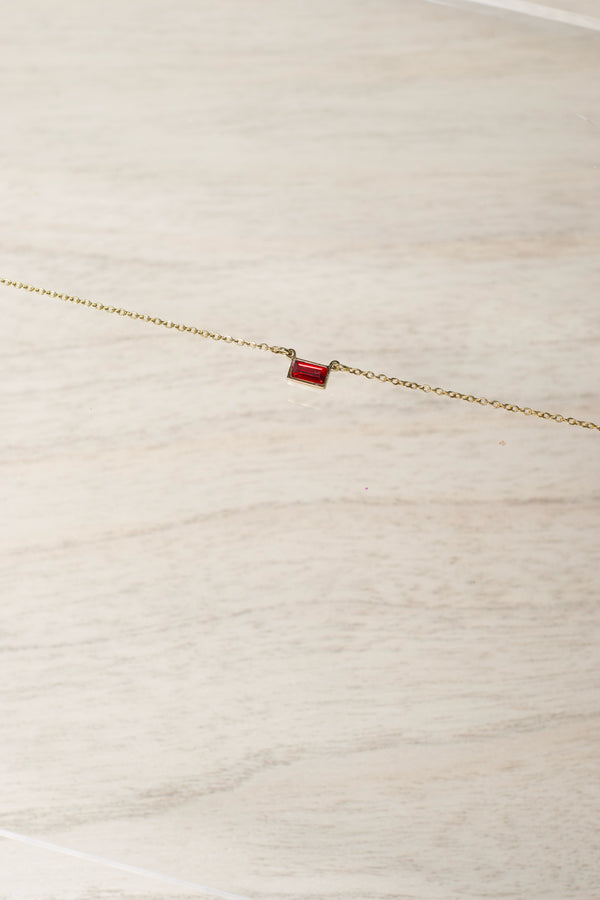 Gold bracelet with a red gemstone on a light wooden surface