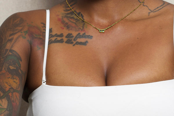 Person with tattoos and a necklace, wearing a white garment.