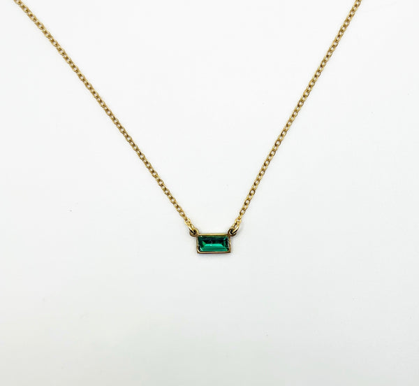 Gold necklace with a green gemstone pendant on a white background