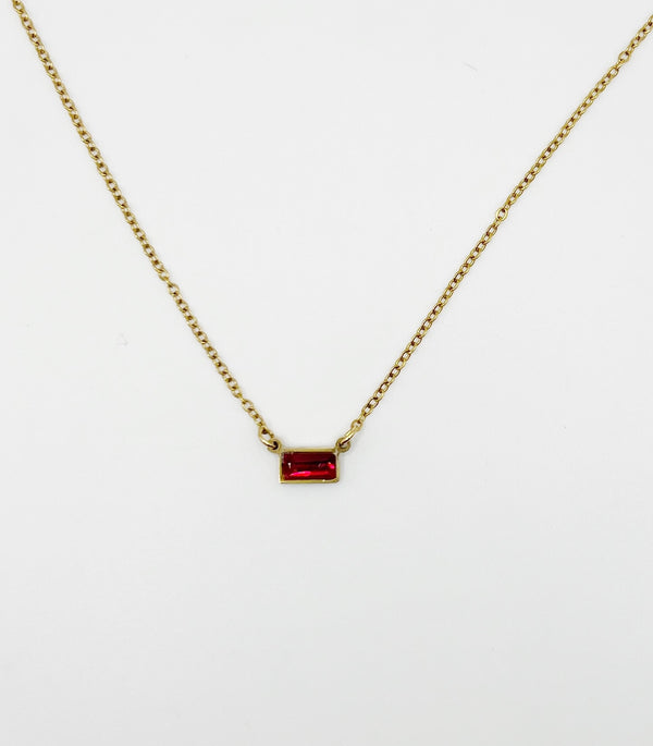 Gold necklace with a red gemstone pendant on a white background