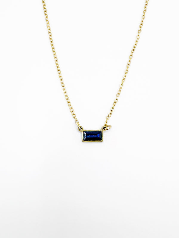 Gold necklace with a blue gemstone pendant on a white background